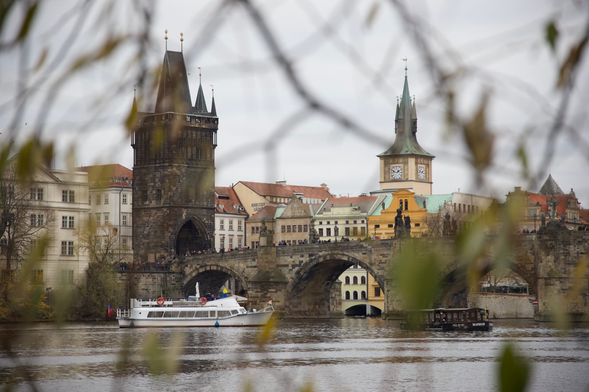 Charles Bridge in Prague seen through branches, boat on the Vltava