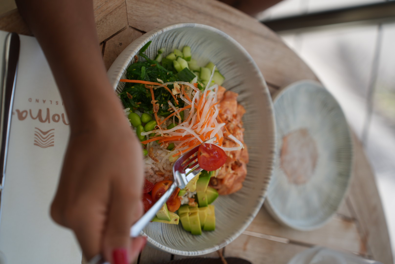 Hands eating a poke bowl at the beach club table